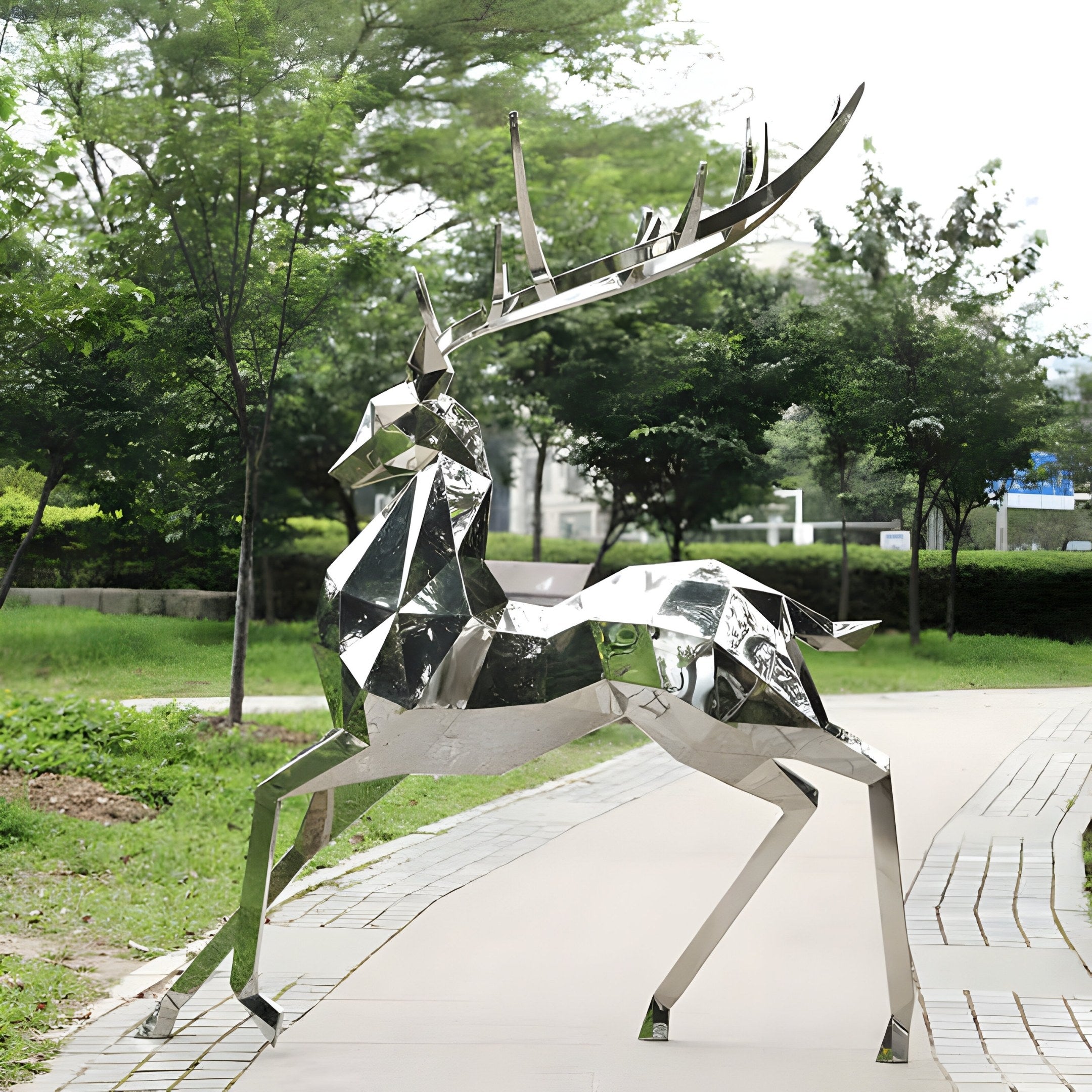 The Noble Deer III Geometric Steel Sculpture by Giant Sculptures, standing at 204cm, graces a paved path. Its polished stainless steel surface beautifully reflects the surrounding greenery and bushes in a park-like environment beneath an overcast sky.