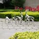 Group of reflective stainless steel deer sculptures displayed outdoors, arranged in a park-like setting with greenery in the background.