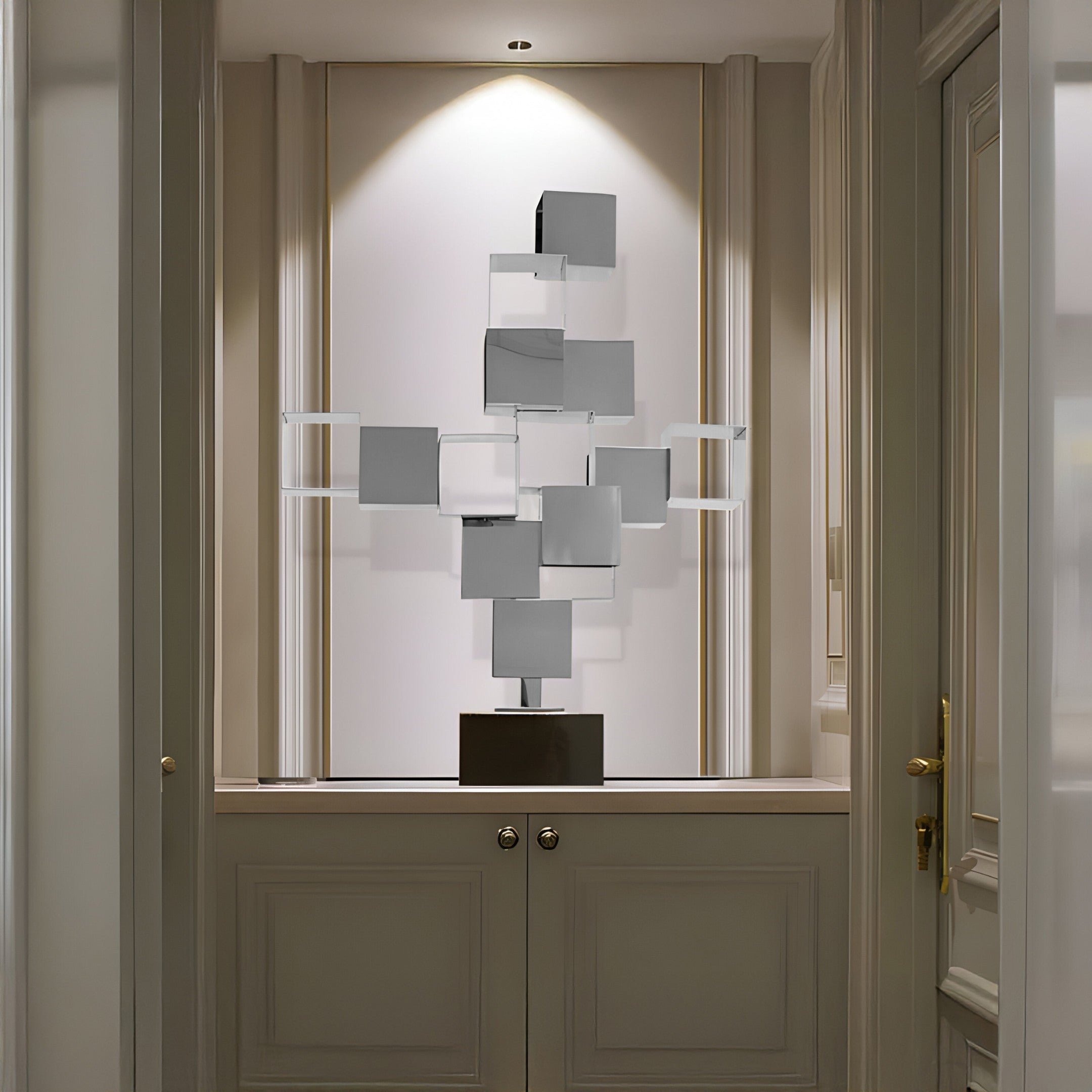 Modern cube-like stainless steel sculpture displayed on a shelf in a dimly lit room, with a focus on the geometric shapes and clean lines.