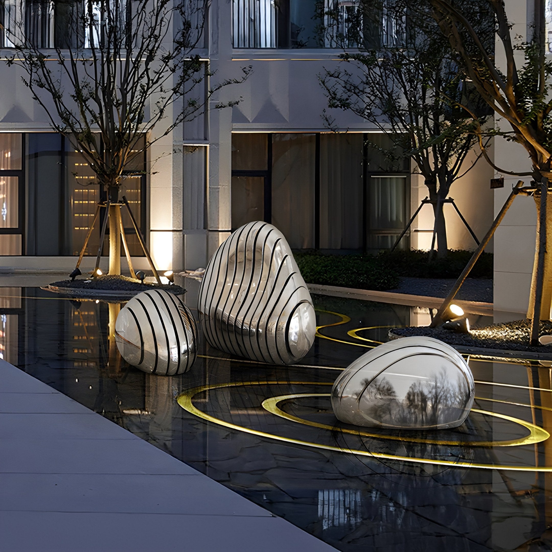 The artistic installation features Giant Sculptures Ripple Silver Organic Outdoor Steel Sculpture (50/95cm), with smooth pebble-shaped forms and black lines on a reflective water surface. Surrounded by trees, modern architecture, and warm lighting, it creates a serene contemporary ambiance.