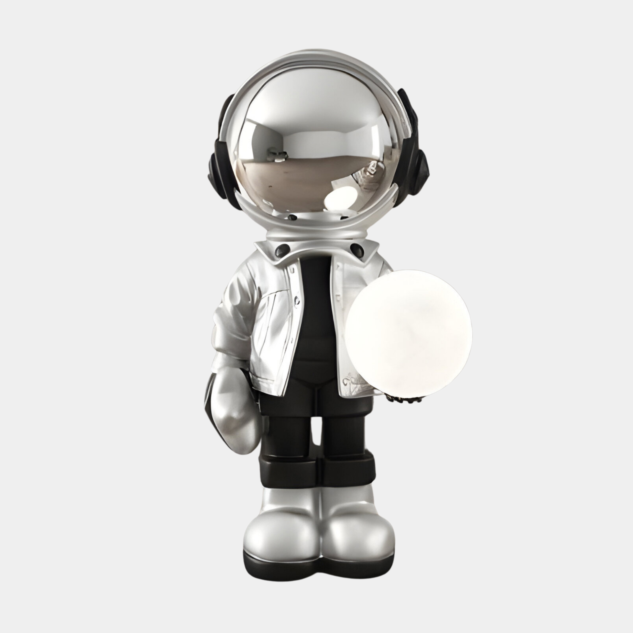 The Lunar Silver Astronaut Glow Orb Sculpture (80cm) by Giant Sculptures is a futuristic figure with a shiny silver helmet and reflective visor, dressed in black pants and boots, holding a glowing white orb in its left hand. Ambient lighting enhances its sleek silhouette against a plain white background.