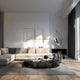 A modern living room showcasing a beige sectional sofa and a round black coffee table with books, enhanced by the stunning Giant Sculptures' Zephyr Silver Abstract Steel Sculpture - 71cm in a polished silver finish. Soft natural light streams through tall curtains, accentuating the minimalist wall design and contemporary aesthetic.