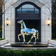 The sculpture displayed in an outdoor space, with the surroundings reflected on its mirrored surface, creating a striking contrast between nature and art.