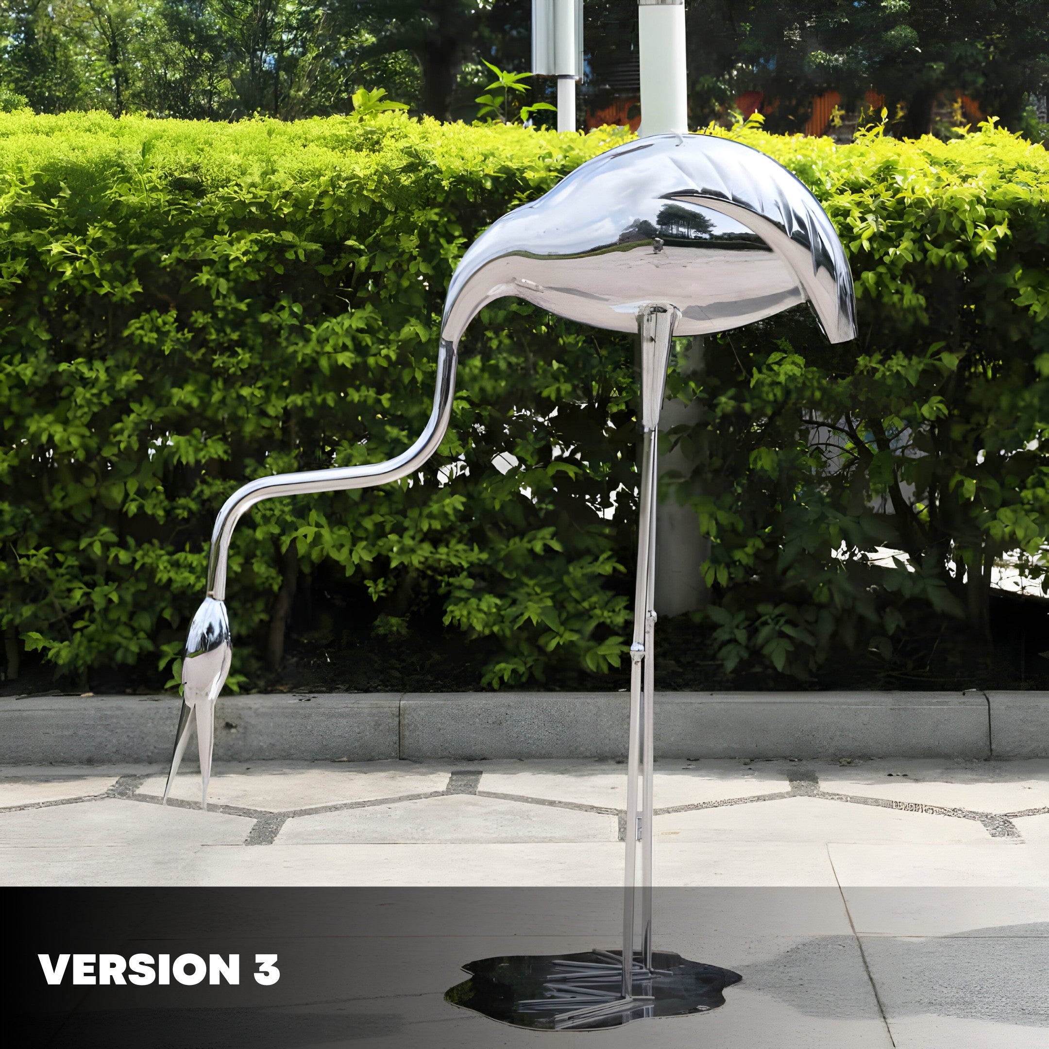 A silver flamingo sculpture with its head lowered, placed outdoors with green hedges in the background, reflecting the surroundings on its shiny surface.