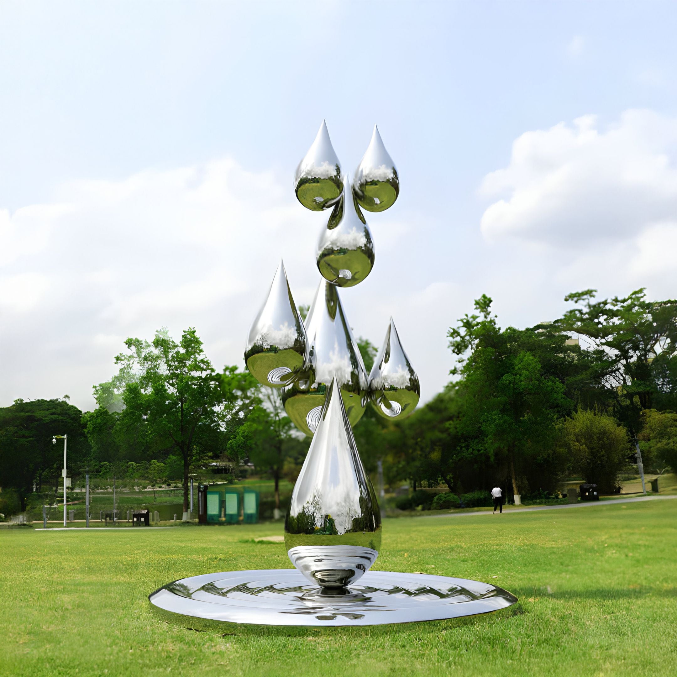 The Raindrop Organic Steel Outdoor Sculpture by Giant Sculptures, standing at 120/220cm, features stacked teardrop shapes in reflective stainless steel. It is displayed outdoors on a grassy field with trees and a cloudy sky beautifully mirrored on its surface.