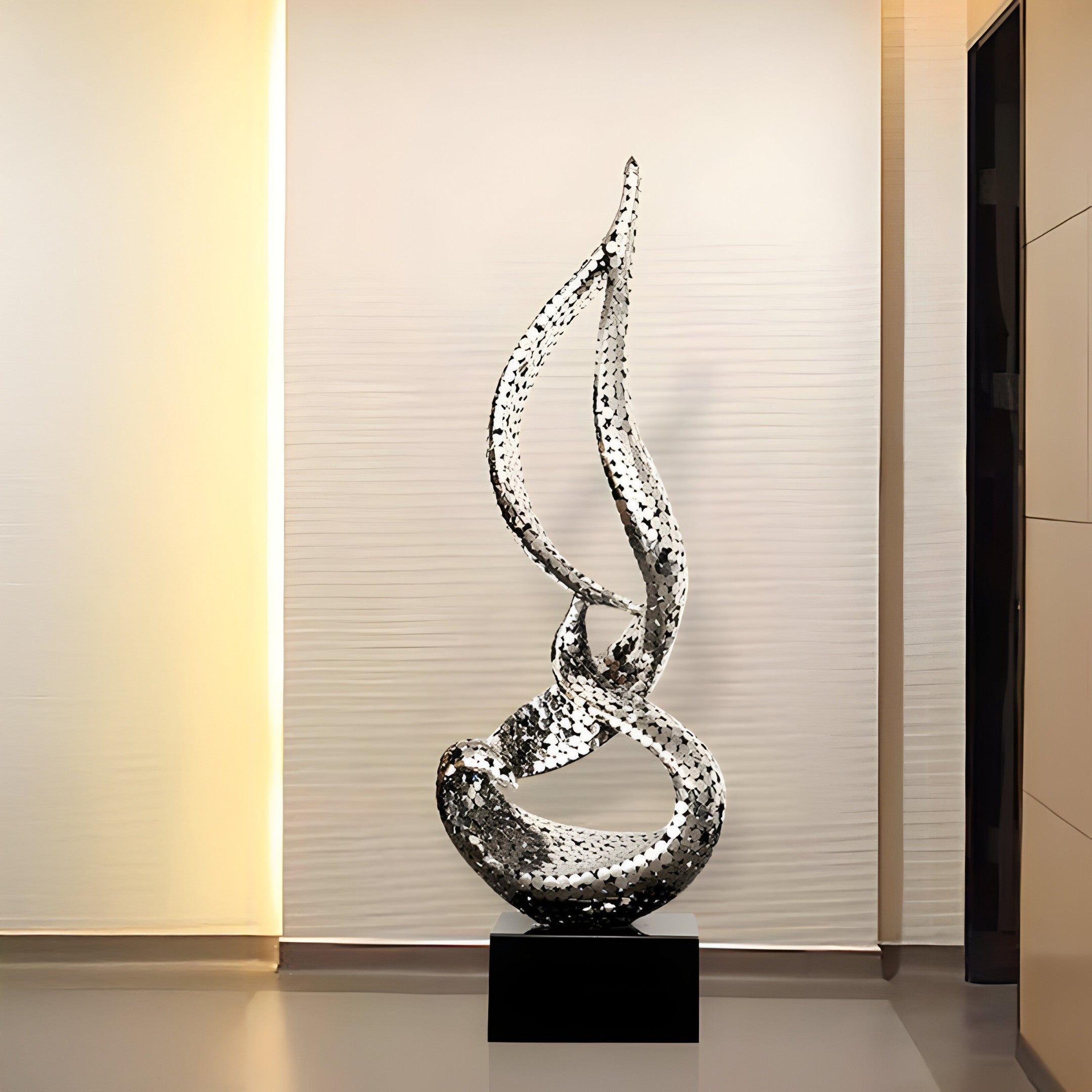 A silver flame sculpture placed in a gallery-style space with warm, ambient lighting.