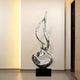 A silver flame sculpture placed in a gallery-style space with warm, ambient lighting.