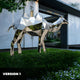 Side view of a silver camel sculpture against a modern building backdrop.