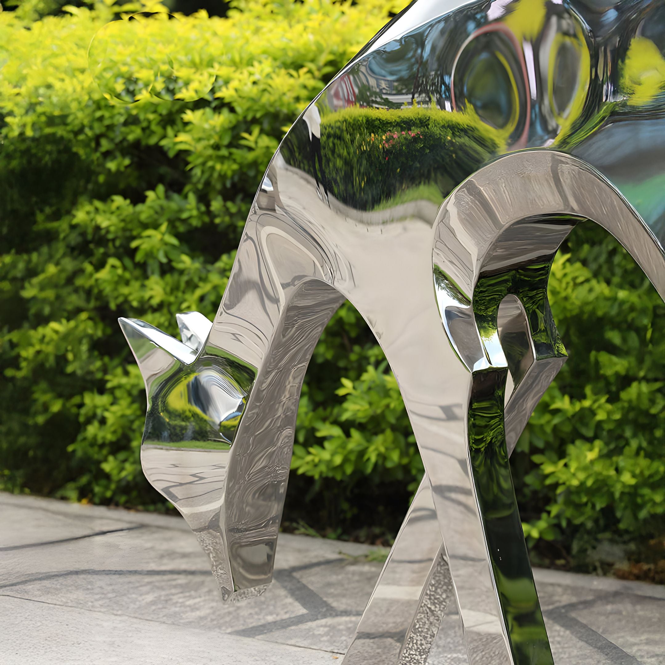 The Deer Organic Steel Outdoor Sculpture by Giant Sculptures, measuring 91/158 cm, enhances an outdoor decor with its polished steel surface reflecting the lush green foliage backdrop.