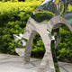 The Deer Organic Steel Outdoor Sculpture by Giant Sculptures, measuring 91/158 cm, enhances an outdoor decor with its polished steel surface reflecting the lush green foliage backdrop.