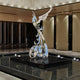 The Phoenix Silver Abstract Outdoor Steel Sculpture - 212cm by Giant Sculptures is a contemporary masterpiece crafted from stainless steel, featuring flowing shapes and wing-like forms. It stands on a reflective base in a sleek setting with dark and light panels, enhanced by subtle lighting.