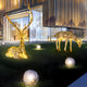 Giant Sculptures' Luminous Stag Gold Steel LED Sculpture, standing at 212 cm, decorates the modern building's outdoor lawn at night alongside glowing orbs. The warm LED lights from the scene cast a golden hue on the windows, with snow-dusted trees reflected in the glass.