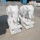 Two Lucky Chinese Elephant II Marble Outdoor Sculptures by Giant Sculptures stand on detailed rectangular pedestals outdoors on a concrete surface. Intricately carved with visible ornamental patterns on their bodies and bases, additional sculptures can be seen in the background.