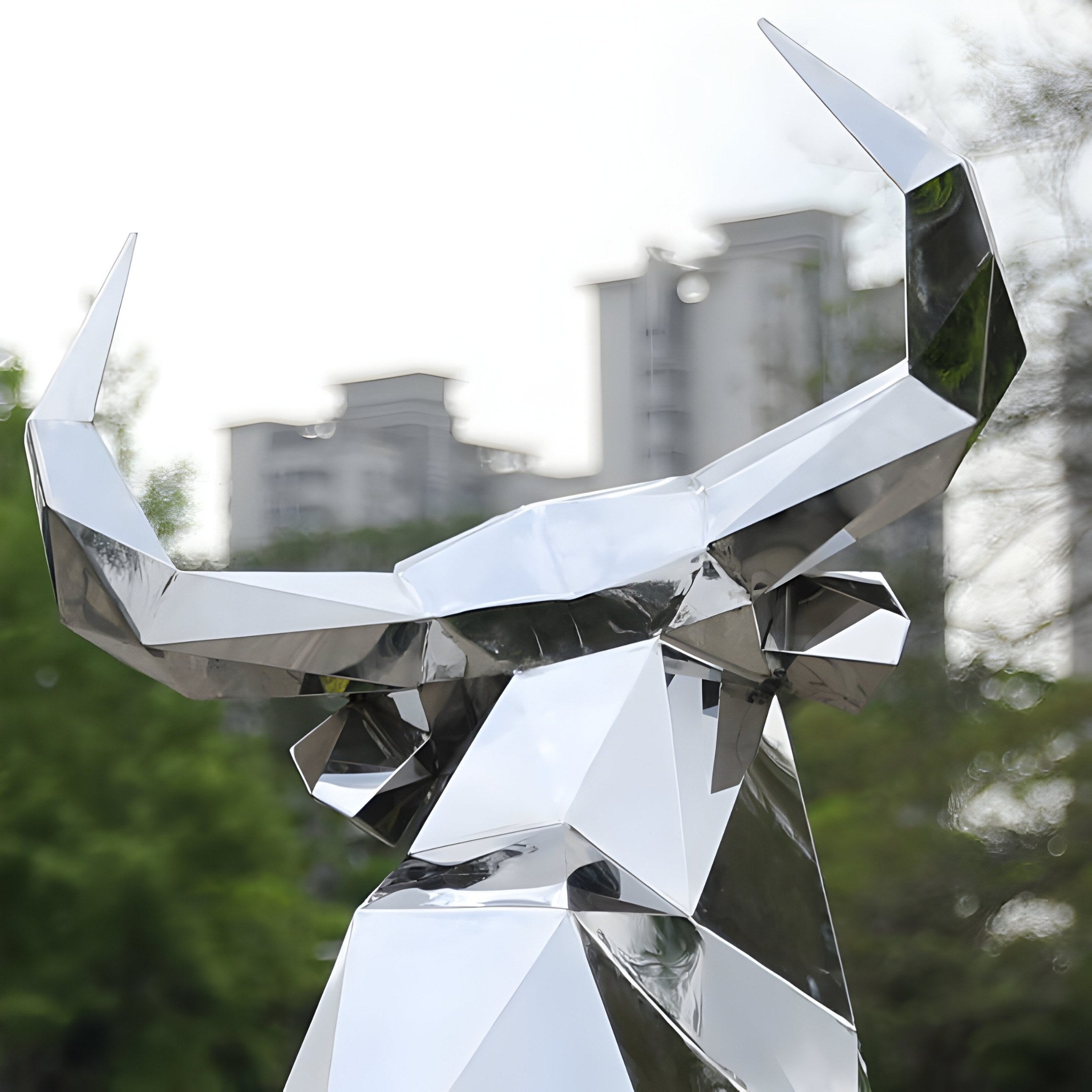 The Bull Geometric Steel Outdoor Sculpture (120/200cm) by Giant Sculptures is a sleek, stainless steel piece with sharp, angular features. It stands outdoors with a polished surface reflecting surrounding greenery and high-rise buildings.