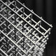 A close-up of a Matrix Silver Geometric Steel Sculpture by Giant Sculptures shows its lattice-like pattern made of intersecting bars and sleek metallic finish, set against a dark blurred background.