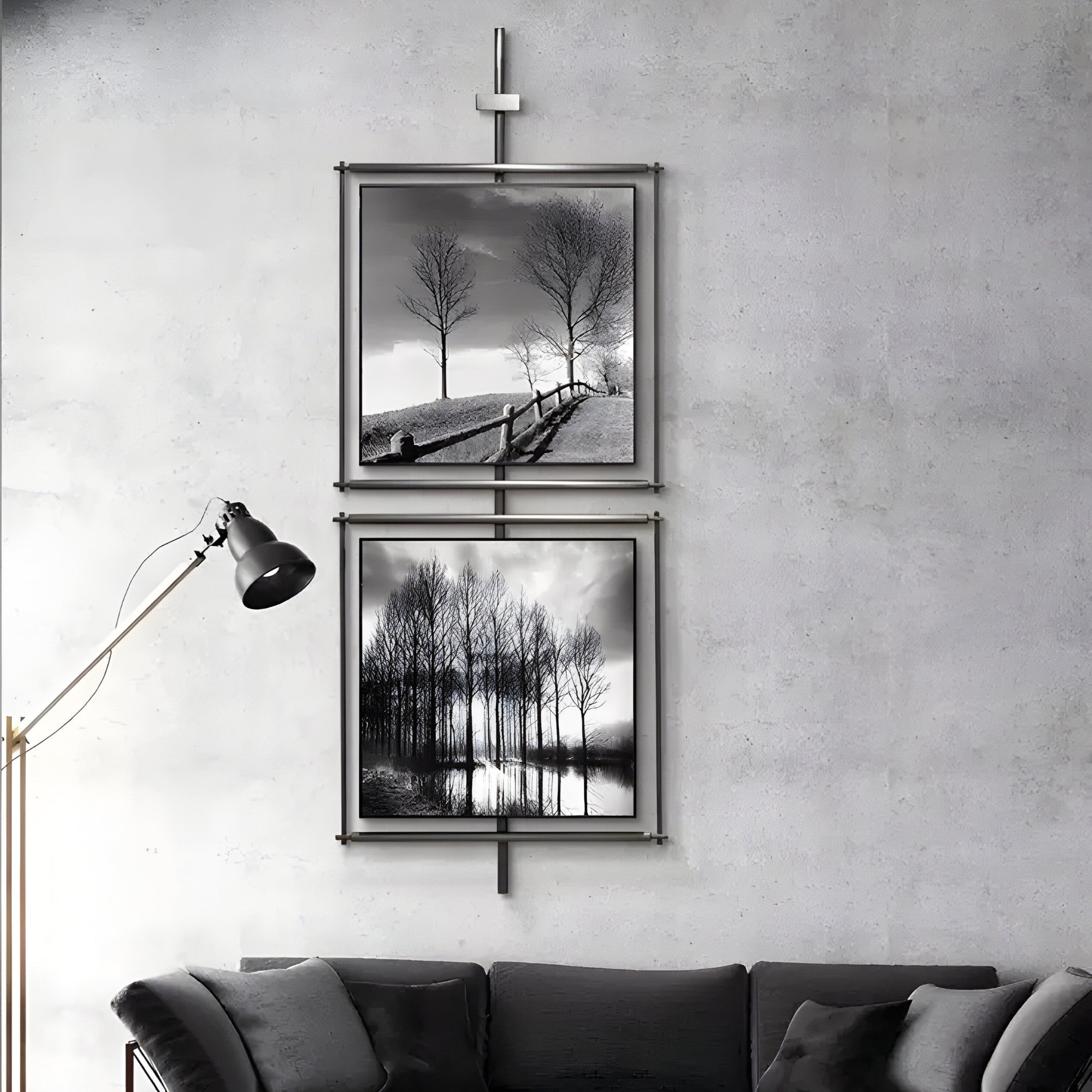 A modern living room features a light gray textured wall with Vistarte Landscapes Abstract Dual Panel Metal Wall Art by Giant Sculptures. Black and white photos depict a tree-lined path and water reflections, while a black floor lamp complements the dark sofa with gray cushions, embodying modern decor.