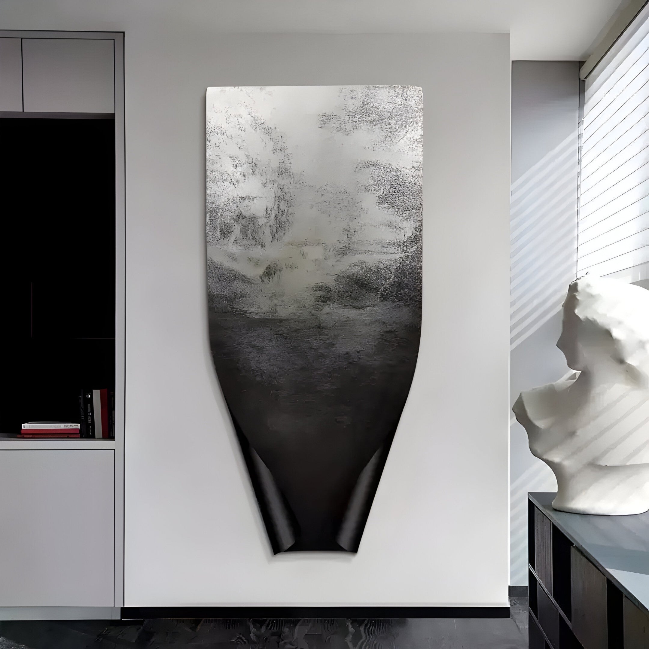 An Echo Mist Landscape Abstract Panel Metal Etched 3D Wall Art by Giant Sculptures hangs on a white wall, shifting from textured silver to smooth black. Nearby, a white abstract sculpture sits on a dark cabinet, illuminated by sunlight streaming through blinds.