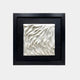 A framed ceramic wall art piece showcasing an abstract design of flowing, wave-like white patterns. The textured ceramic sculpture has layered, undulating curves that resemble ripples or draped fabric, adding depth and movement.