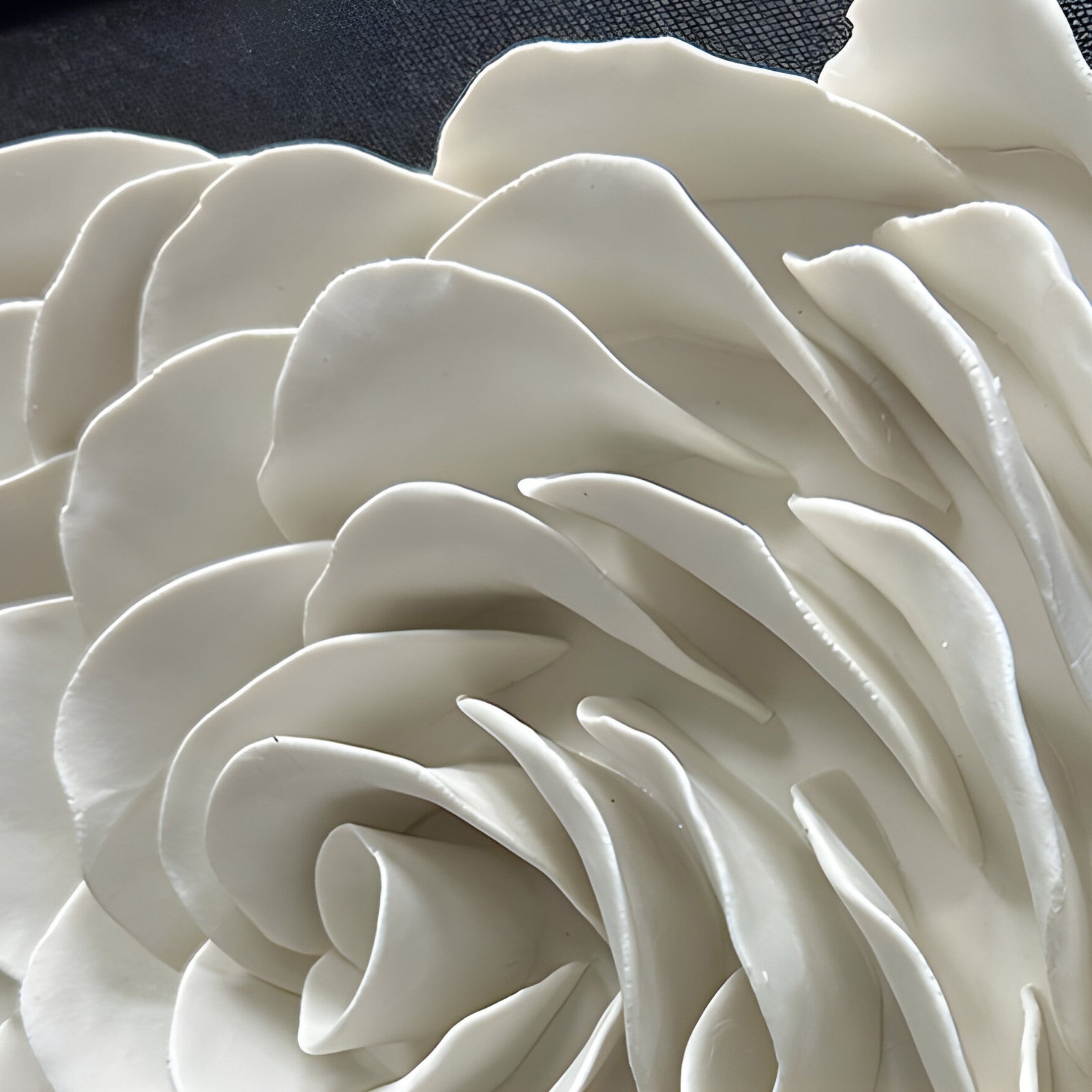 Detailed close-up of layered white ceramic petals forming a delicate, rose-like pattern in a modern abstract wall sculpture.