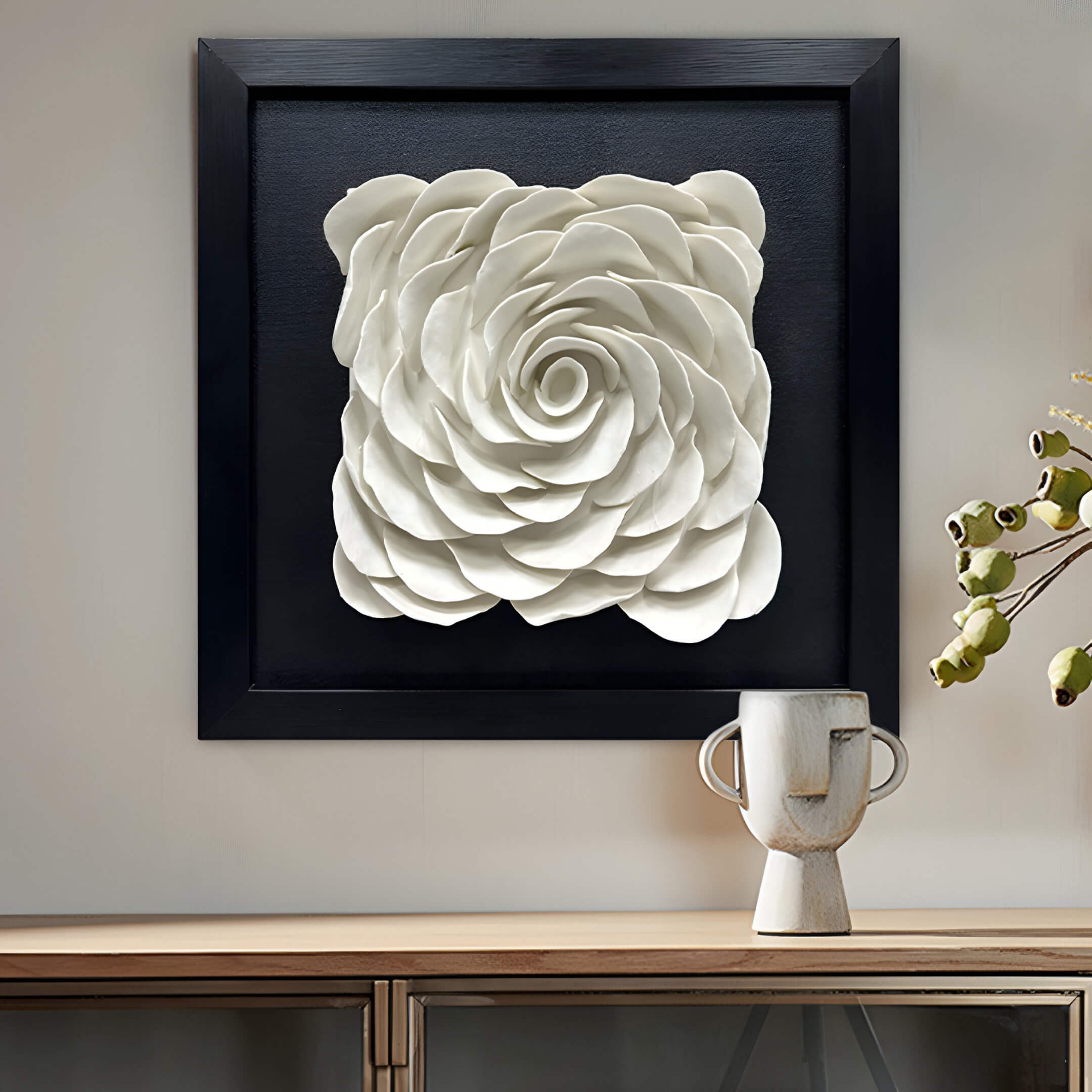 The Harmonia 3D Rose Wall Installation from Giant Sculptures, with a black frame and white sculptural design, makes a modern floral statement on a light backdrop. Below it, a minimalist ceramic vase is elegantly showcased on the wooden shelf.