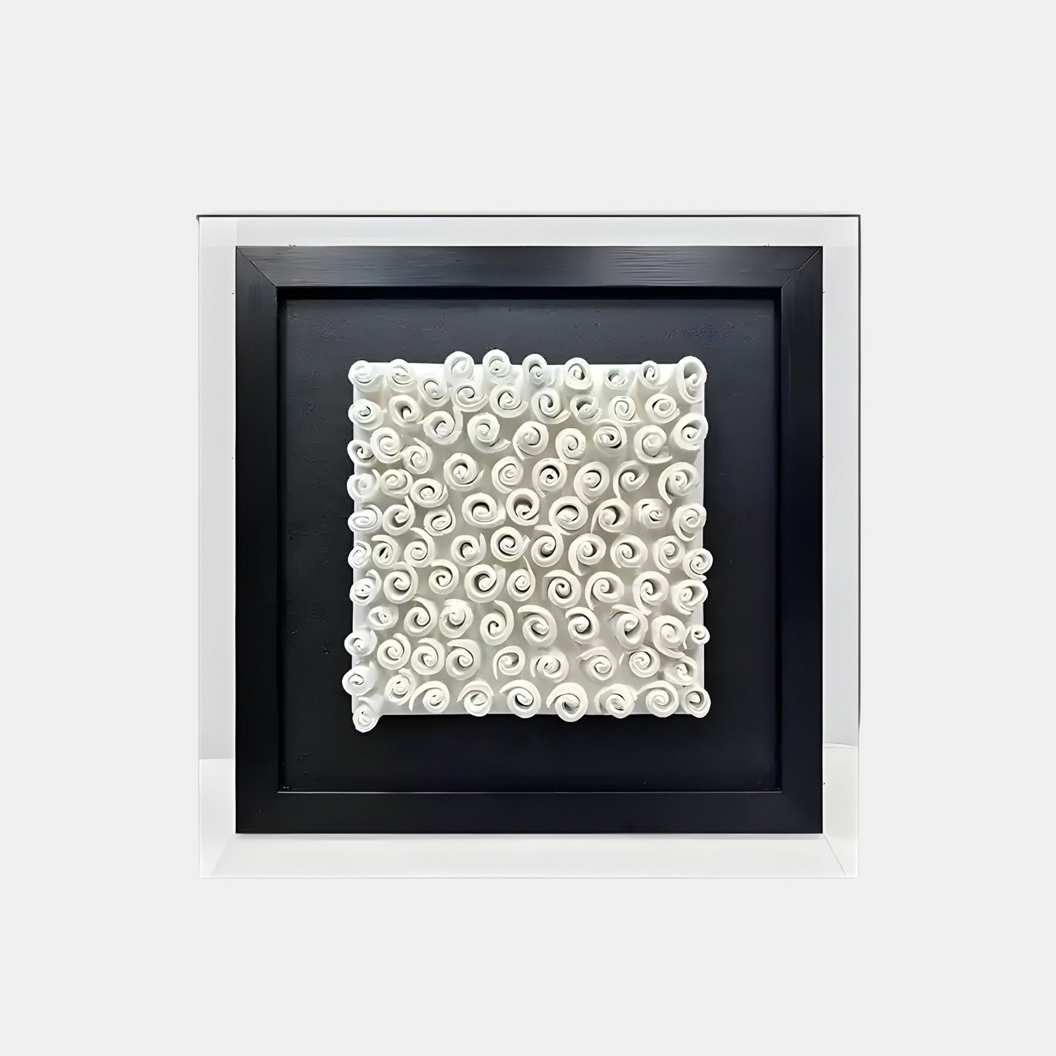  A framed 3D wall art piece featuring a textured design composed of tightly curled white spirals arranged in an organized grid. The spirals resemble rolled scrolls or shells, creating a dynamic, uniform pattern. The artwork is set against a black background and framed with a sleek black border.