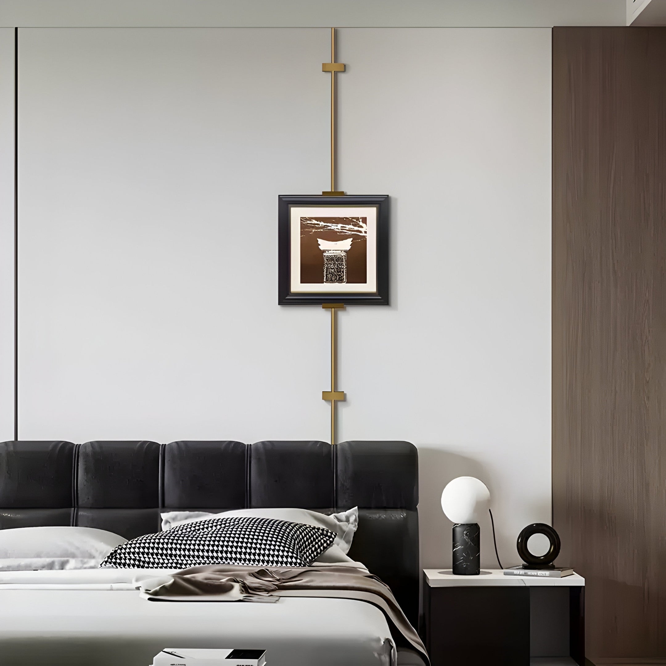 A contemporary bedroom features a black leather headboard and patterned cushions. On the bedside table, theres a spherical lamp and decorative item. Above the bed, Giant Sculptures Ecliptica Abstract Architectural Column Gold Frame Wall Art adds elegance to the minimalistic wall.