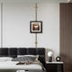 A contemporary bedroom features a black leather headboard and patterned cushions. On the bedside table, theres a spherical lamp and decorative item. Above the bed, Giant Sculptures Ecliptica Abstract Architectural Column Gold Frame Wall Art adds elegance to the minimalistic wall.