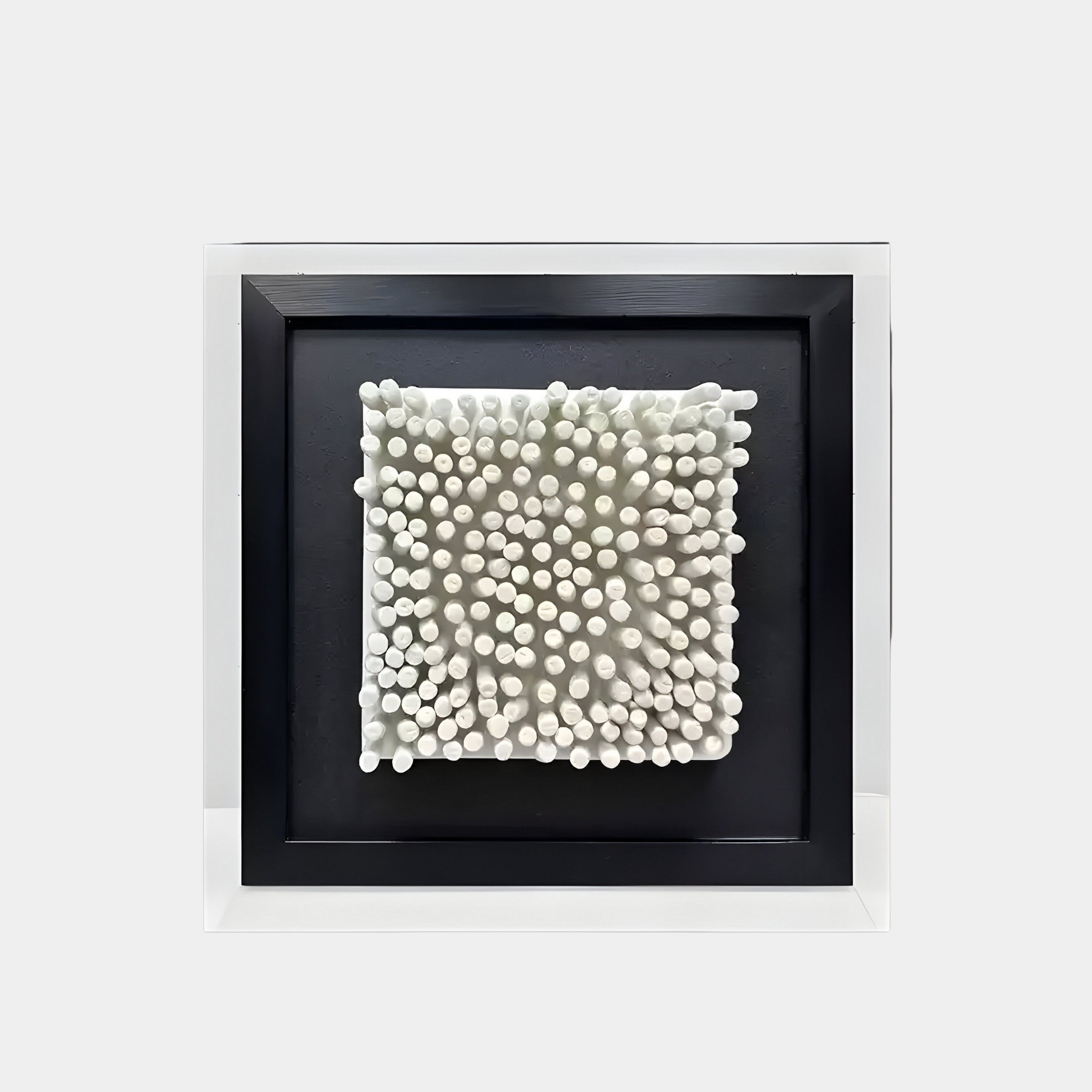 A framed 3D wall art piece featuring an array of white cylindrical protrusions arranged in varying heights, creating a dynamic, textured effect. The cylindrical elements resemble clustered rods or spikes and are set against a black background, framed in a sleek black border.