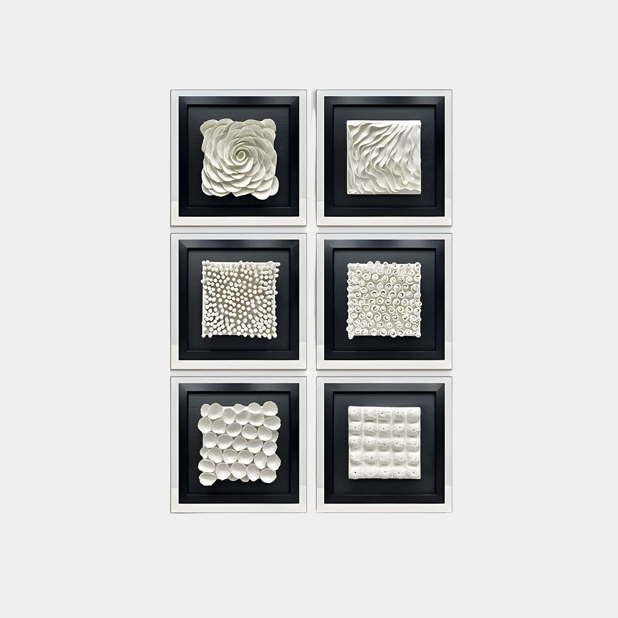  A collection of six framed 3D wall art pieces arranged in a vertical grid. Each frame contains a unique textured white sculpture set against a black background. The designs include spirals, waves, rounded petals, clustered spheres, and other intricate, abstract patterns. The sleek black frames unify the artwork into a cohesive and visually striking display.