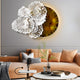 A modern living room has a beige sofa with cushions. Above, the Aurum Flora White Petals Amber Metal Wall Art by Giant Sculptures adds elegance with its white lace-like flowers and warm golden-brown circle. A small table is home to a decorative figurine and plant.