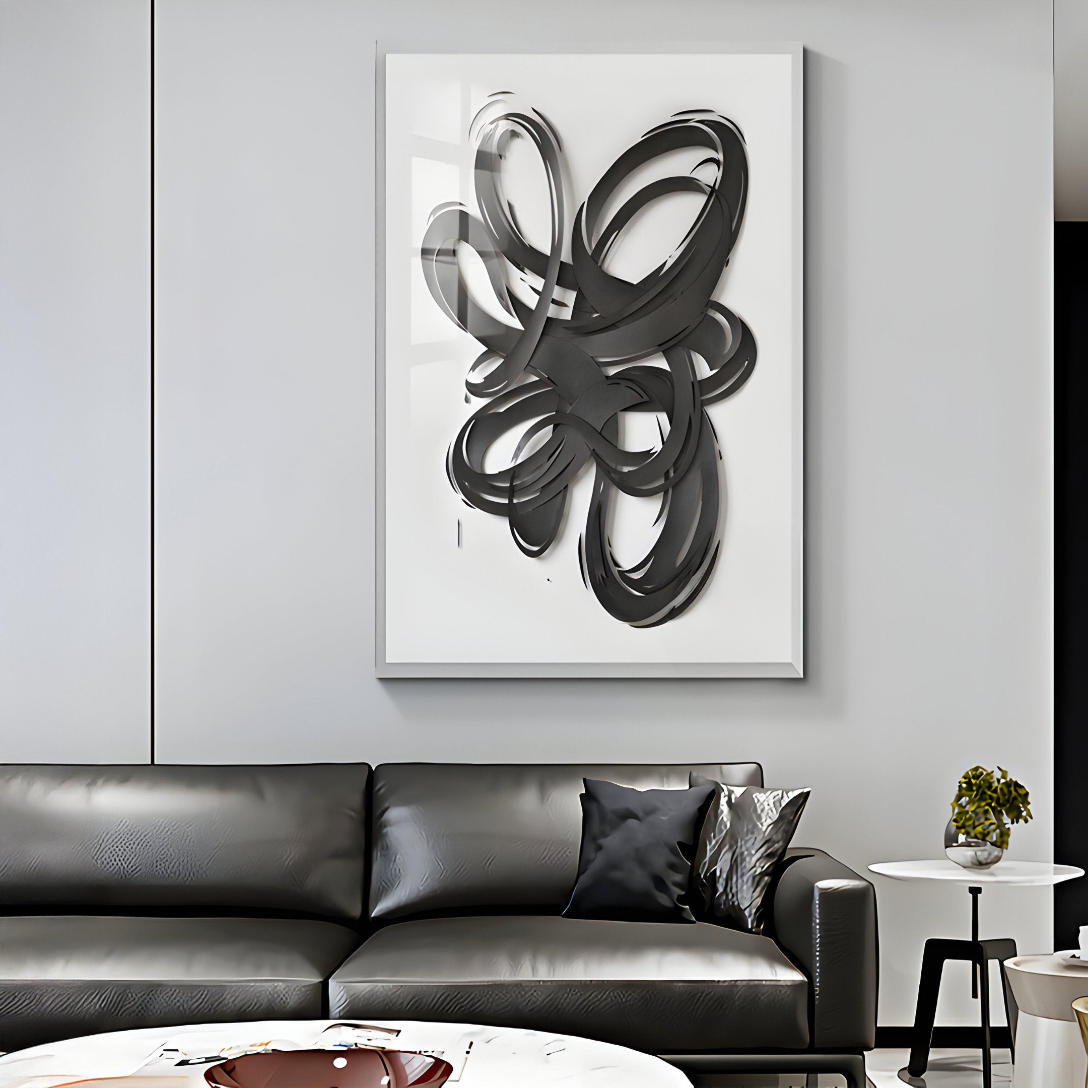 A modern living room features a black leather sofa with a dark pillow. The ambiance is elevated by the Zephyr Black Cascade Abstract Metal Wall Art from Giant Sculptures. A nearby small side table with a plant completes the minimalist look.