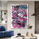 In a modern living room, the Scriptura III Multicolour Graffiti Expression Metal Wall Art by Giant Sculptures showcases vibrant overlapping words in black, pink, and blue on the wall. A sleek blue couch pairs with a glass vase of dried plants in the foreground, while a mirror adorns the left wall for urban chic reflection.