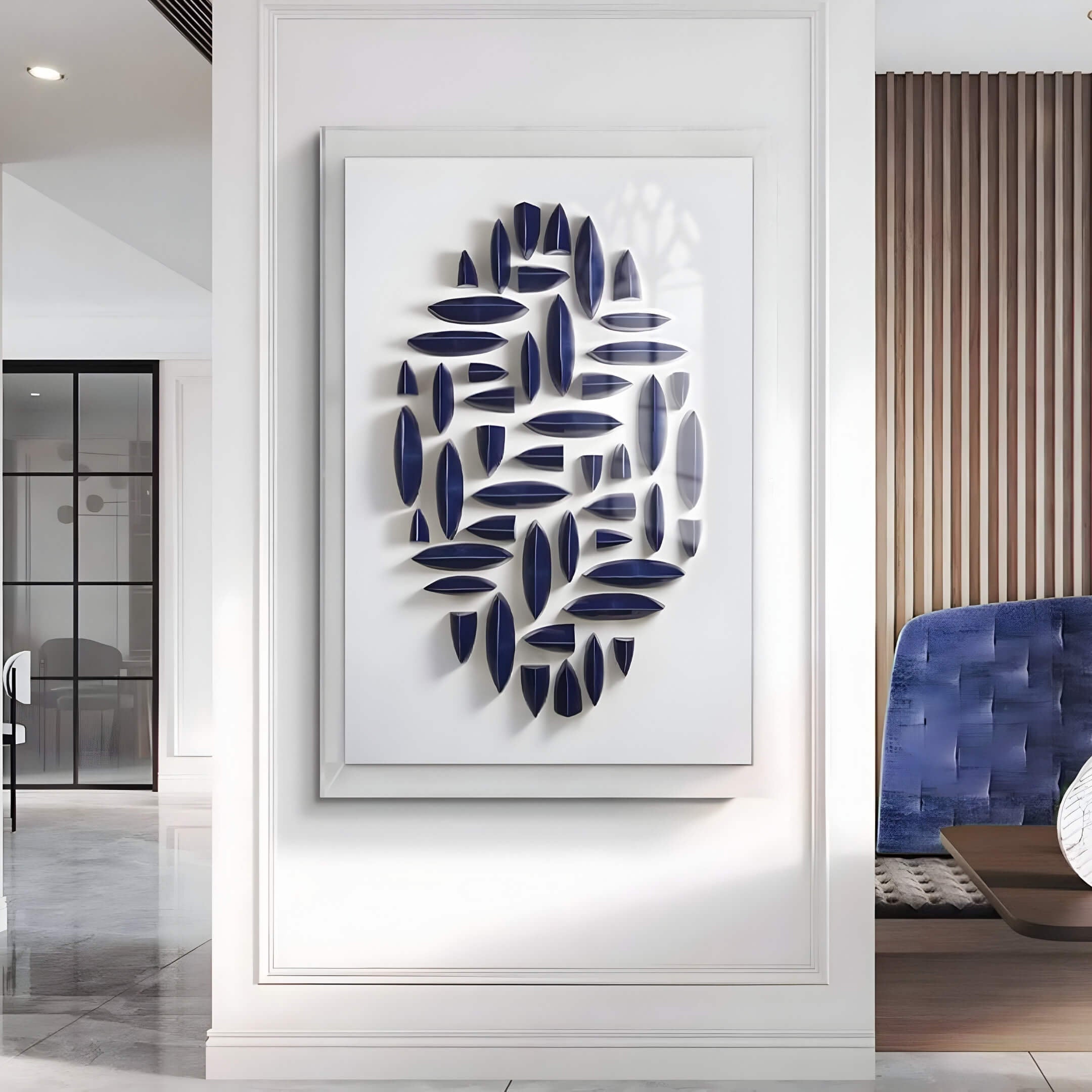 A modern interior features the Elysian 3D Ceramic Wall Art by Giant Sculptures, showcasing navy blue, elongated leaf-like shapes in an abstract pattern on a large white wall. The room includes a polished floor, glass partition, and blue cushioned chair.