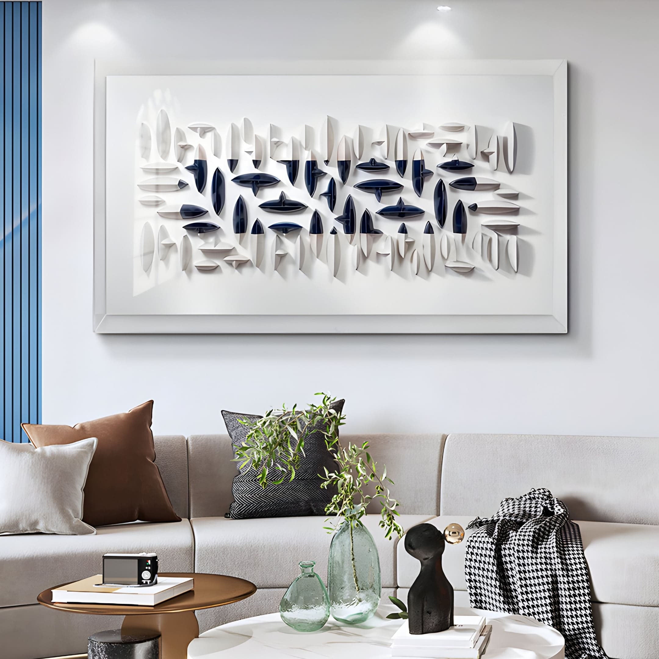 A modern living room features a light gray couch with white, brown, and gray pillows and a white coffee table showcasing decorative items. On the wall, there is Giant Sculptures Elysian 3D Ceramic Wall Art in navy blue and white abstract design.