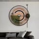 The Circulo Modern Kinetic Metal Wall Art by Giant Sculptures, featuring geometric patterns and a sleek right-swinging pendulum, enhances a modern industrial vibe above a dark sofa decorated with grey and white pillows.