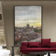 The Vista Sunset Urban Landscape Carving Wall Art by Giant Sculptures features an urban scene with a distant pagoda under a cloudy sky, sunset hues, and complements the modern elegance of a room decorated with a burgundy sofa, matching pillows, and sleek side tables.