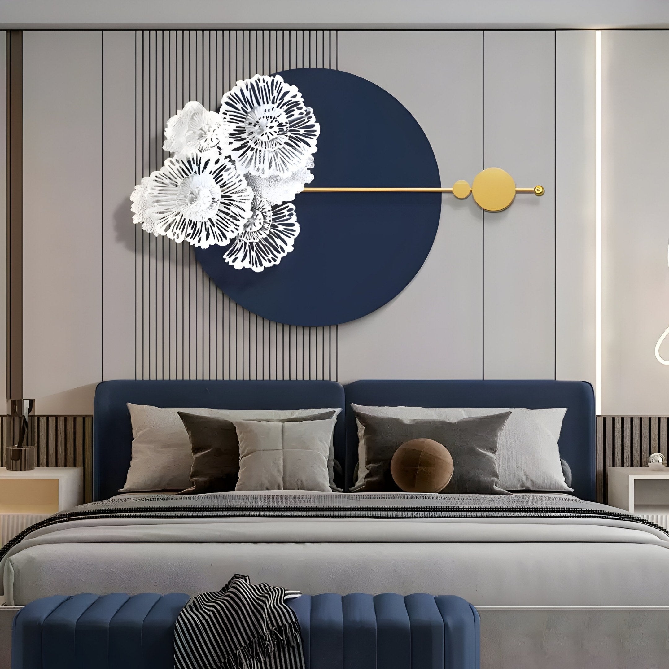 A modern bedroom features a dark midnight blue bed with gray and black pillows topped by a striped throw. Above, the Blossom Halo Midnight Blue Round Floral Decorative Wall Art by Giant Sculptures hangs, complementing the sleek, neutral walls and furnishings.