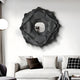 A modern living room features a white couch with black and white pillows. Above it, the eye-catching Sculptura Mirror Charcoal Grey Floral Round Metal Wall Art by Giant Sculptures adds interest. A floor lamp with a round white shade complements the sleek decor in the corner.