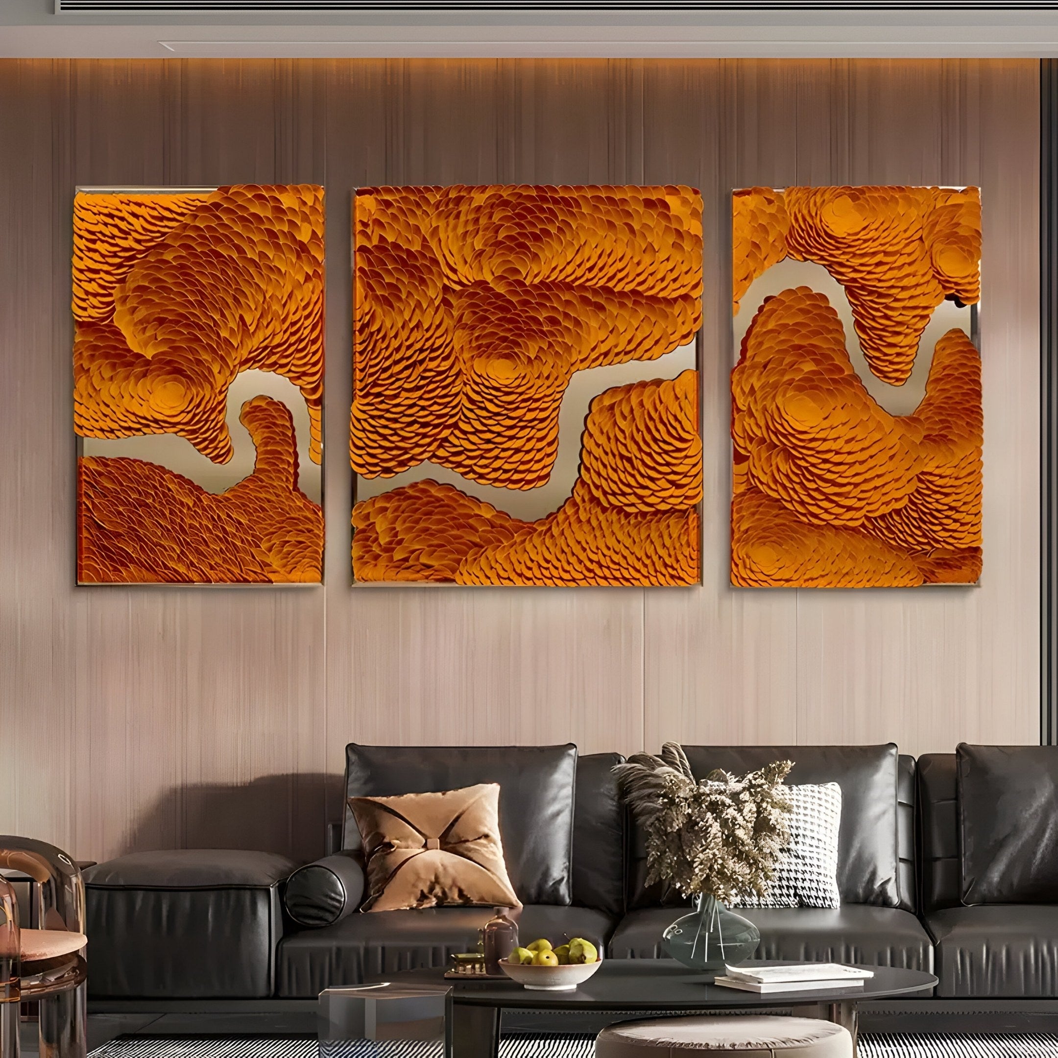 A modern living room boasts a black leather sofa with pillows and a throw blanket. Above it hangs the Giant Sculptures Riverine Flow Golden Orange Textured Triptych Wall Art, featuring abstract swirls. A coffee table in front completes the stylish setting.