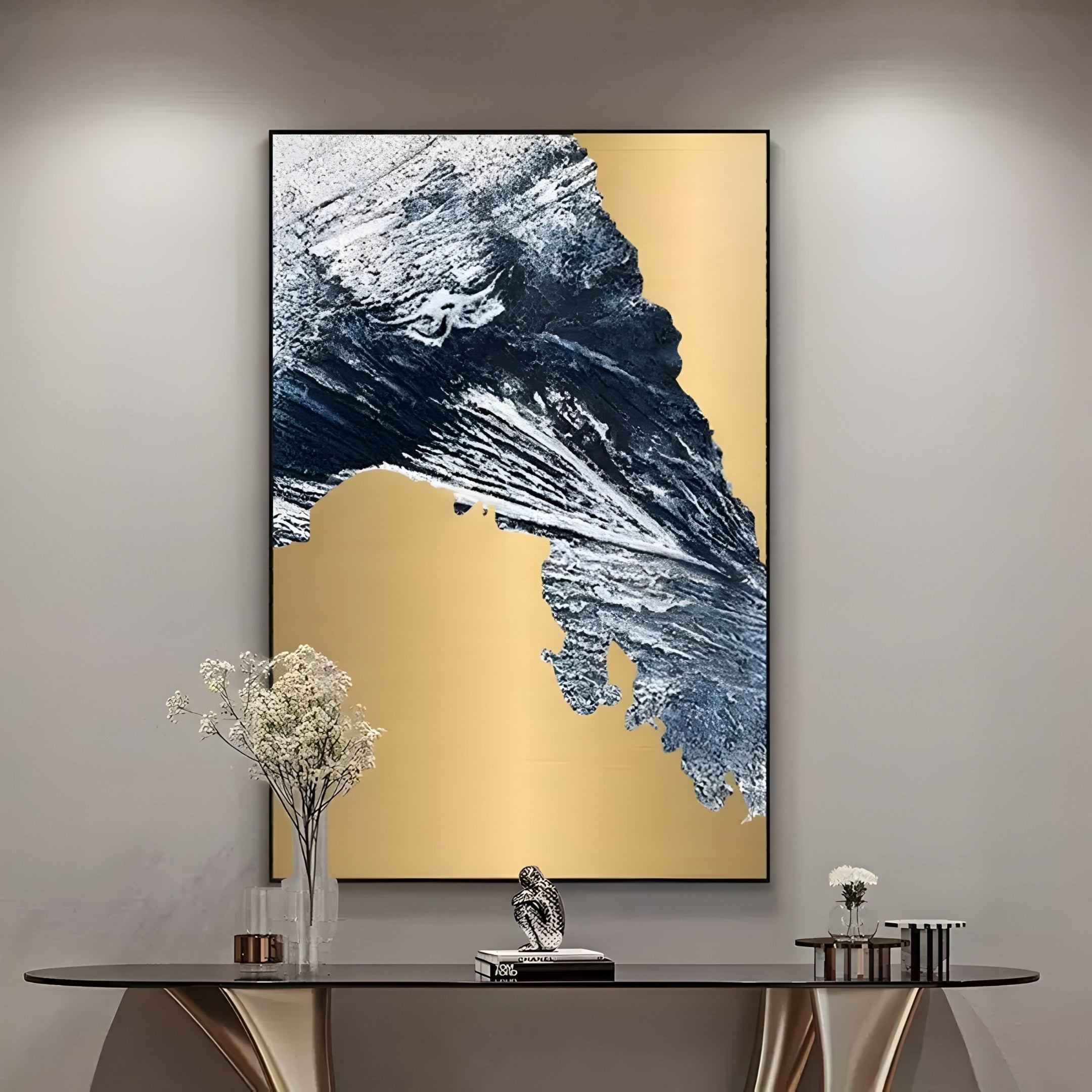 In a modern living room, the Terranica Golden Terrain Abstract Metal Wall Art by Giant Sculptures shines with rich gold and blue tones above a sleek console table. The table features decorative elements like small plants and a spiral sculpture, embodying contemporary design.