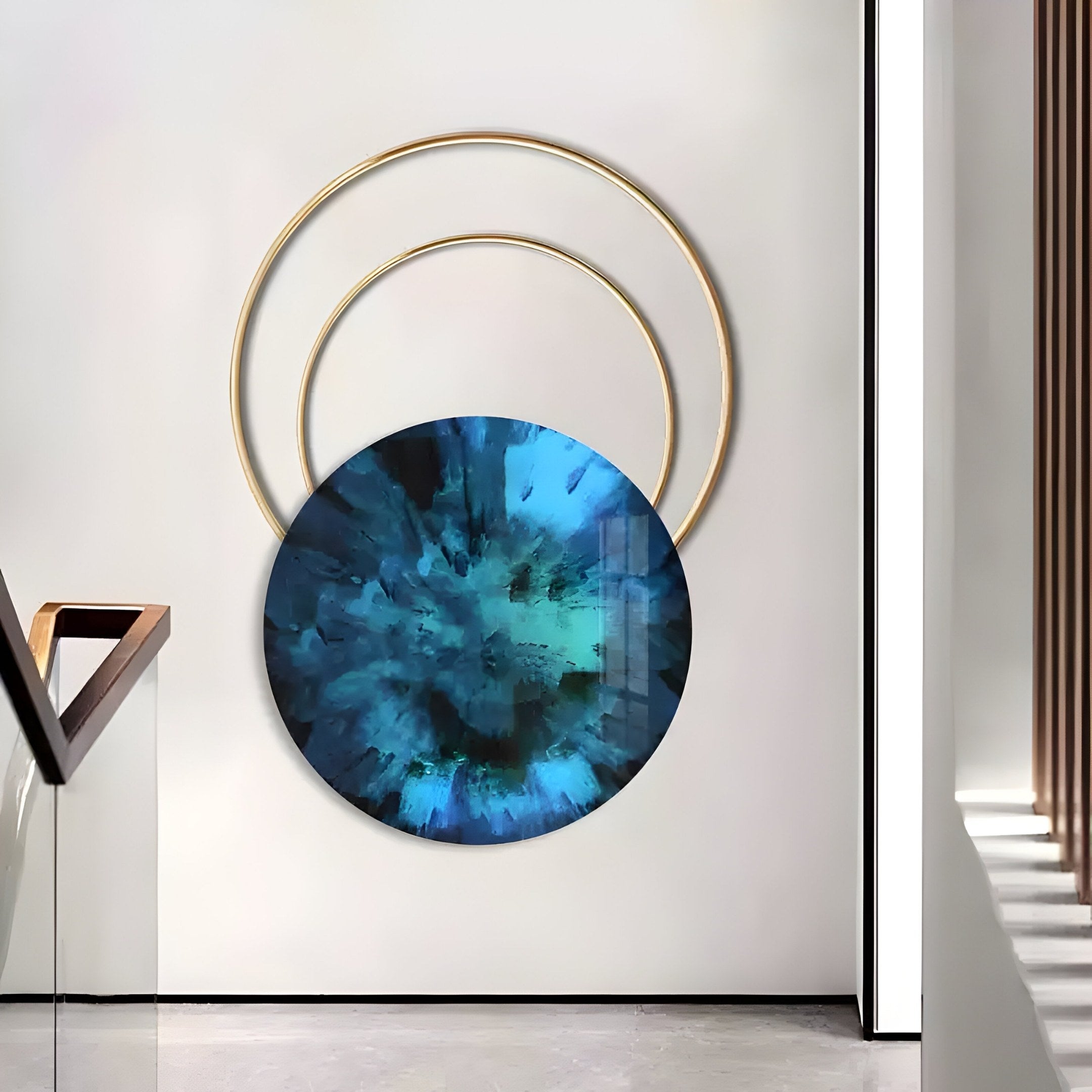 A modern art installation by Giant Sculptures features the Eclipse Luxe Azure Radiance Circular Ring Wall Art: a large, round azure painting with eye-like textures, encircled by overlapping golden rings. Mounted on a white wall in a minimalist space, it embodies contemporary interior elegance.