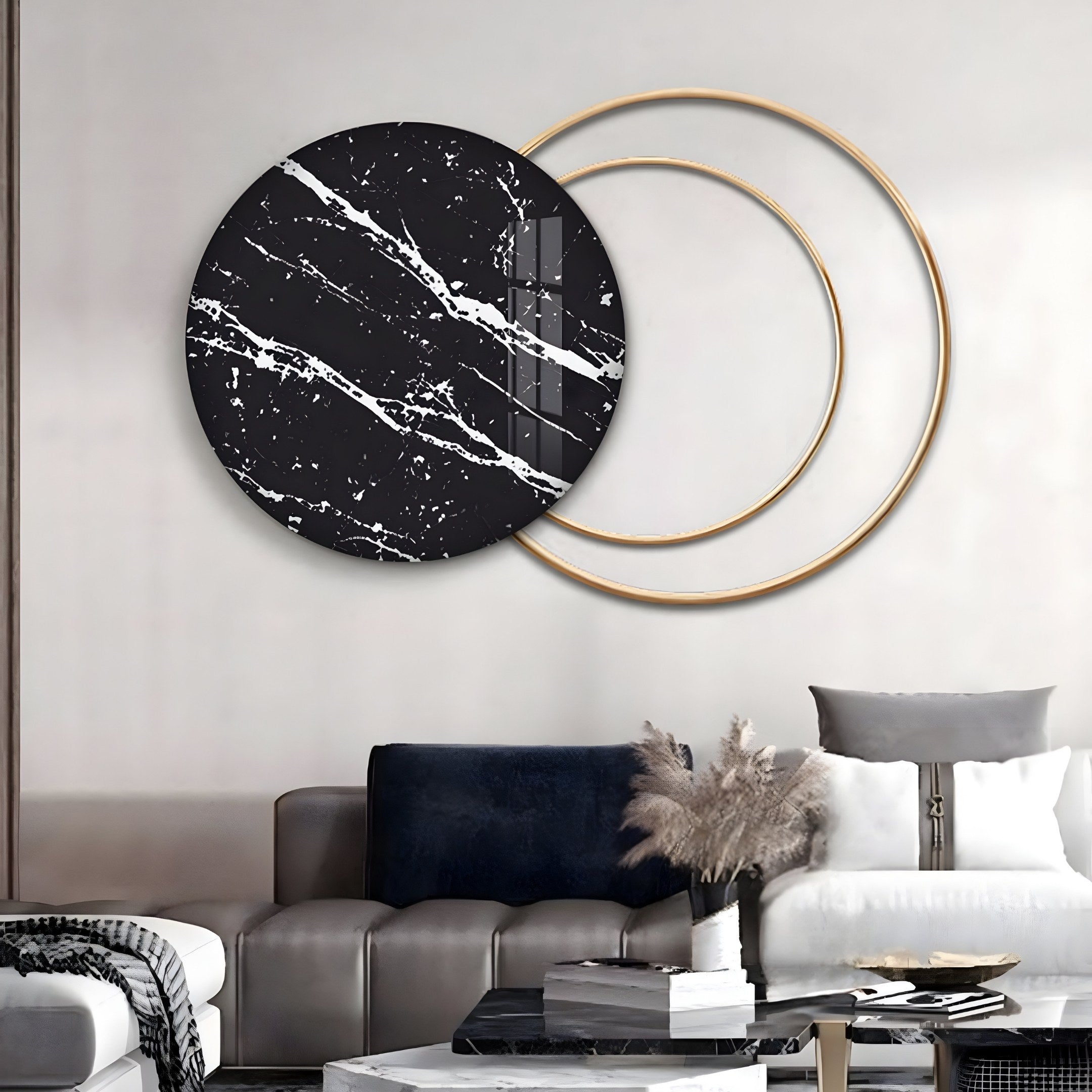 A modern living room showcases a beige sofa with black and white pillows, complemented by a small black coffee table. Above the sofa, Giant Sculptures Eclipse Luxe Black Noir Marble Circular Ring Wall Art adds a touch of elegance. Pampas grass in a vase decorates the table.