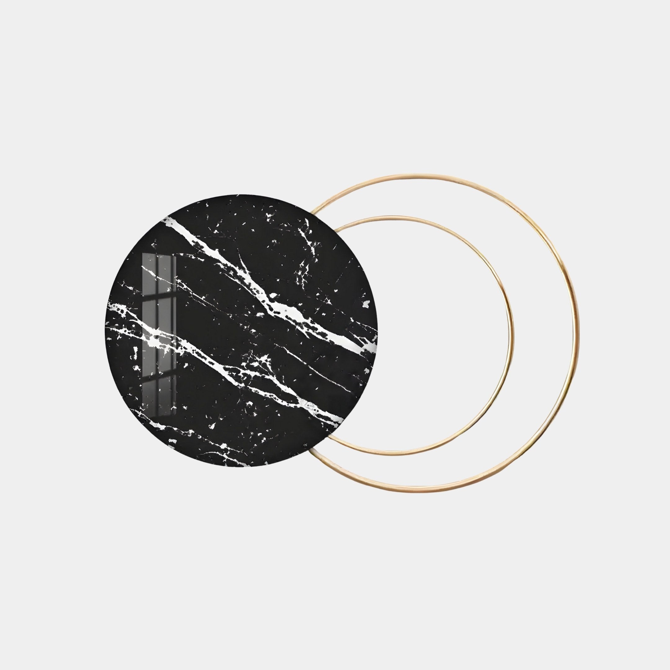 The Eclipse Luxe Black Noir Marble Circular Ring Wall Art by Giant Sculptures showcases a modern design, with a black marble circle featuring white veins that elegantly overlaps two thin gold rings on a pristine white background, offering an off-center visual interplay for captivating appeal.