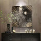 A modern room features Giant Sculptures Astralis Bronze Cosmic Drift Abstract 3D Wall Art, centered by a silver sphere. Below it, a sleek black console showcases green branches in a vase, abstract white sculptures, and stacked books for an elegant contemporary look.