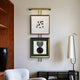 A modern living room showcases a white armchair, a black shelf with books, and a tall lamp. Above the shelf are two Artisera Monochrome Symphony Minimalist Dual Frame Built-In Light Wall Art by Giant Sculptures, featuring geometric designs. A wooden accent adds warmth to the space.