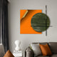 The Tesselle Orange Metal Fold & Green Textured Geometric Wall Art by Giant Sculptures, with its abstract design, enhances the space behind a gray sofa featuring bold cushions. A unique white lamp sits on books near gray curtains beside the sofa, echoing the wall arts colors.