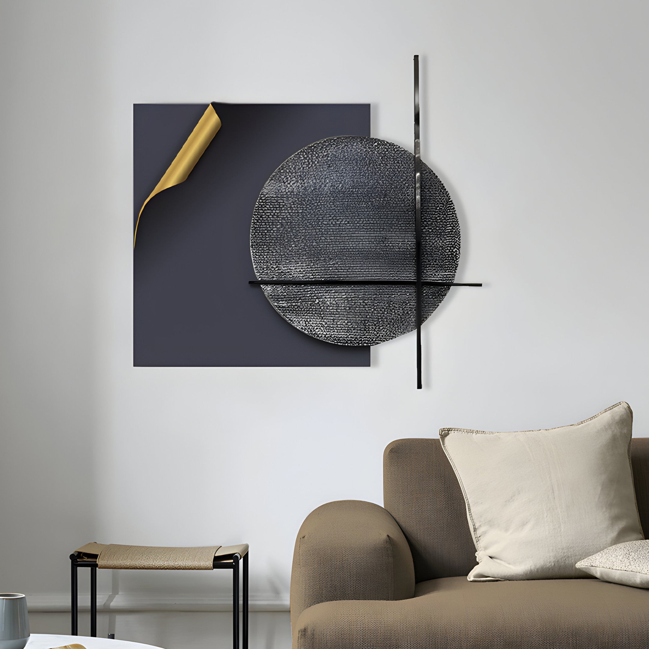 A modern living room features a beige couch with cushions, accentuated by Giant Sculptures Tesselle Black Metal Fold & Grey Textured Geometric Wall Art, showcasing a dark square with golden edges and intersected circles embodying minimalism. A small table sits next to the couch.