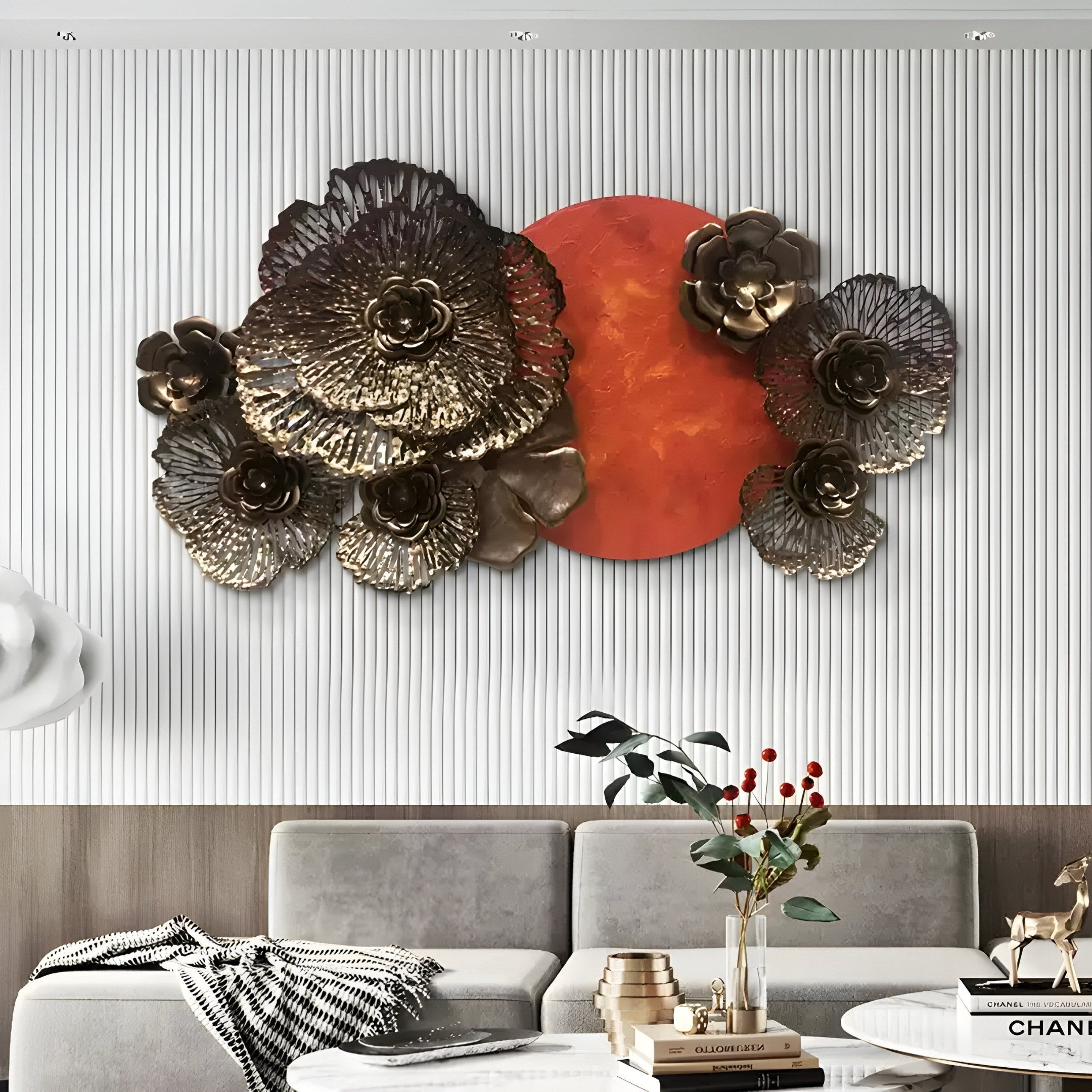 A modern living room showcases the Luminis Bloom Red Floral Metal Wall Art by Giant Sculptures, with a red circular centerpiece. Below is a gray sectional sofa, partially revealing a coffee table decorated with a vase of red berries and metallic accents.