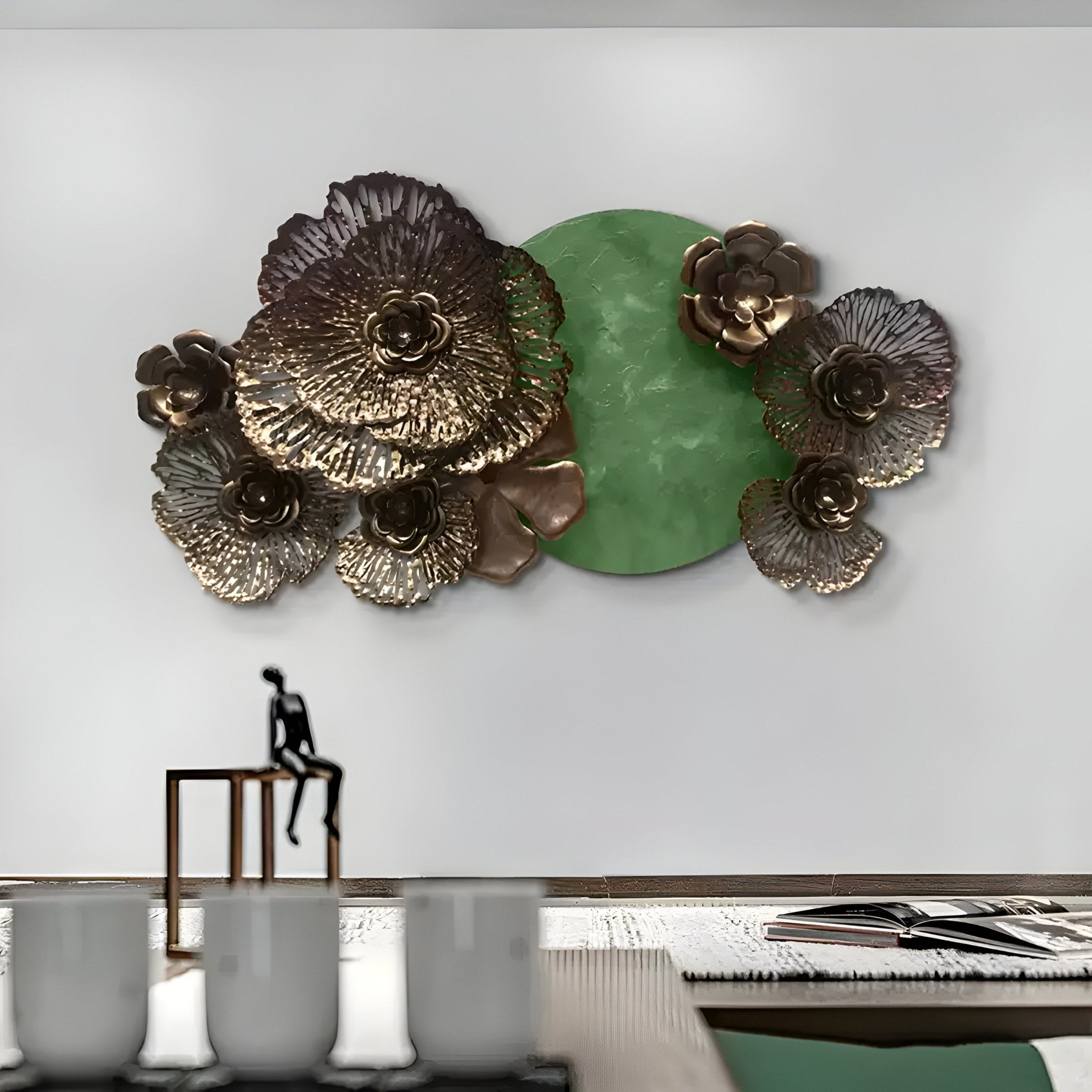 The Luminis Bloom Green Floral Metal Wall Art by Giant Sculptures blends modern design with natures charm, featuring metallic flowers around a green circle against a white wall. A small person sculpture sits on a wooden ledge, while three white cups and an open book grace the table below.