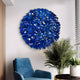 A modern living room highlights the Eclat Sphere Blue Abstract Metal Wall Art by Giant Sculptures above a blue velvet chair, capturing cobalt tones. A tall potted plant stands next to a window with horizontal blinds, while partial wood paneling enhances the cohesive modern design.